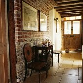 Antike Stühle und Konsolentisch im Eingangsflur eines rustikalen, alten Landhauses mit Ziegelmauern und Kalksteinfliesen