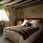 Doppelbett mit Webpelzdecke und Teddy in niedrigem Landhaus-Schlafzimmer mit Holzbalkendecke