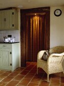 Rattansessel auf Terrakotta-Bodenfliesen in einer Landhausküche mit braunem Türvorhang