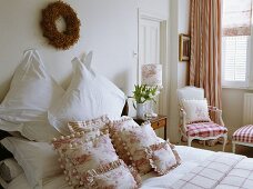 Zweigkranz über dem Bett mit weißen Kissen und rosa und weißen Toile de Jouy Kissen im traditionellen weißen Schlafzimmer