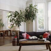 Ein rustikaler Holztisch, große Dracaena Zimmerpflanzen und eine Couch, neben der ein Fass als Ablage benutzt wird, richten das Wohnzimmer ein