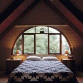 Ein Loft Schlafzimmer mit einem halbkreisförmigen Fenster und beidseitigen Dachschrägen