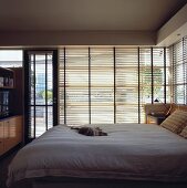 Holz Jalousien sind vor den großen Fenstern angebracht worden und sorgen in einem Schlafzimmer für Sichtschutz, in dem eine Katze auf dem Bett schläft