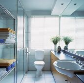 weiße Jalousien sind vor dem Fenster oberhalb der Toilette angebracht worden, die in einem kleinen Bad steht, das mit einer Edelstahlkonstruktion für Handtüchern und einem großen Spiegel eingerichtet worden ist