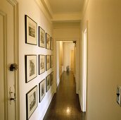 Schmaler, langer Gang mit weißen Wänden, einer Sammlung schwarz-weisser Bilder und einem grauen Fussboden