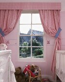 Rot weiss karierte Vorhänge neben Sprossenfenster darunter Rattanstühlchen mit Spielsachen im Kinderzimmer