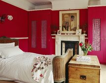 Traditionelles Schlafzimmer in Rot mit antikem Bettgestell aus Geflecht vor Kamin