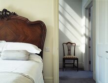 An antique bed next to an open door and a view of a chair in a hallway