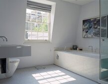 A white designer bathroom with stone tiles on the bathtub and white mosaic floor tiles