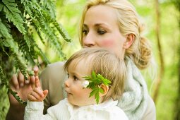 A mother and child looking at ferns in a forest