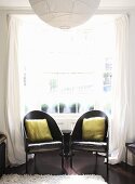 Two black armchairs in front of a Georgian bay window with white curtains