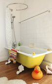 A giant rubber duck in front of a yellow bathtub with a shower and a shower curtain