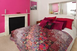 Ein Doppelbett mit Dekokissen und einer Tagesdecke in einem Schlafzimmer mit pinkfarbenen und weissen Wänden