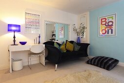 Ein dunkelblaues Sofa mit Dekokissen, ein Bodenkissen und ein weisser Schreibtisch in einem Wohnzimmer