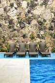 A pool with loungers against a natural stone wall