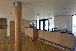 Open kitchen with wooden kitchen units in the living room with wood clad columns and wood flooring