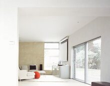 Open designer living room with white sofa and sideboard next to a window with a partially opened blind