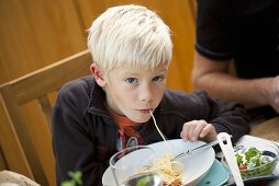 A blond boy eating spaghetti