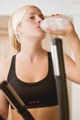 Blonde Frau trinkt Mineralwasser beim Training