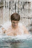Junger Mann steht unter einem Wasserfall