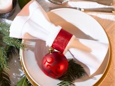 Place-setting with white napkin, red bauble and fir sprig