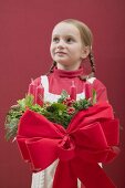 Kleines Mädchen hält Adventskranz mit roter Schleife