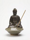 Incense stick in ceramic dish in front of Buddha figure