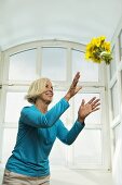 Senior woman catching bunch of flowers, smiling, low angle view