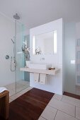 A modern bathroom in white with a basin, a glazed shower area and brown wooden inlays in the tiled floor