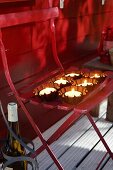 Lit tealights in small cake moulds on folding chair outside