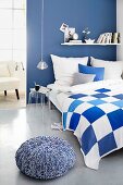 Blue and white bedroom with plexiglass bedside table and pouffe with knitted cover