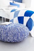 Pouffe with knitted cover and blue and white checked bed linen in bedroom