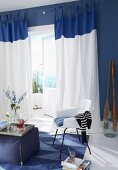 Wohnraum in Blau & Weiß mit Sitzecke aus Stoffhocker & Stuhl vor Balkontür mit bodenlangen Vorhängen