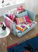 An armchair with colourful, floral-patterned cushions, a retro side table and a patterned rug in a living room