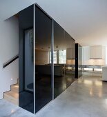 Black, high-gloss built in cupboard in the hallway in front of staircase on a polished concrete floor