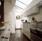 Kitchen with skylight strips above a white lacquered hanging cupboards and stainless steel oven on dark wood flooring