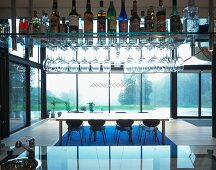 Bar mit Spirituosen und Gläsern auf abgehängtem Regal und Blick auf Esstisch vor Glasfassade