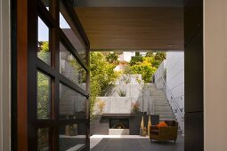Blick durch offene Terrassentür auf moderne Terrassenanlage mit Sessel vor Aussenkamin