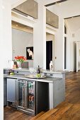 A kitchen counter with a fridge in an open-plan living room with a rustic parquet floor
