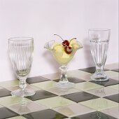 Various retro-style stemmed glasses, one filled with dessert on chessboard patterned tiles