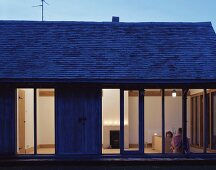 Schlichtes Einfamilienhaus mit Terrassenfenster und Blick in beleuchteten Wohnraum
