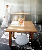 Blurred woman in front of reflective stainless steel fitted cupboards in sunny dining area with 50s-style wire mesh chairs