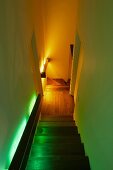 Walls of narrow, winding stairway with landing illuminated in different colours by indirect handrail lights behind wooden cladding