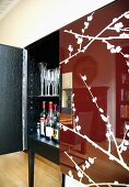 Spiegelung des Wohnzimmers in glänzend rotbrauner Tür mit Blütenzweigmusterung an halb geöffneter Schrank-Bar