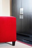 Red upholstered stool in front of reflections in handle elements of black, modern wooden cupboard