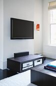 Small, abstract painting and wall-mounted flat screen TV above black audio cabinet