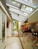Glasdach über langer Küchenzeile mit reflektierenden Lichtspots auf Edelstahl-Arbeitsplatte