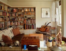 Youthful living room in natural colours with bookcases, guitar and artist's mannequin next to modern table lamp with transparent shade