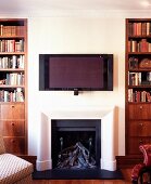 weiße Wand mit Flachbildfernseher über offenem Kamin zwischen traditionellen Bücherregalen