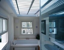 Light and shade effect through horizontal blinds covering large skylight in modern bathroom with English sash windows